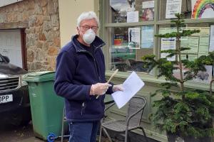 John Davies is seen (with mask) holding a wooden spoon. Trefonen Post Office restricts the number of customers in the shop to 2 by using wooden spoons to gain entry ie only 2 spoons outside shop to designate whether entry permitted or not!
