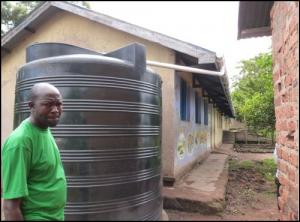 Mr Francis Olowo, deputy Head teacher, with the water tank and the 40 m of guttering used to fill it