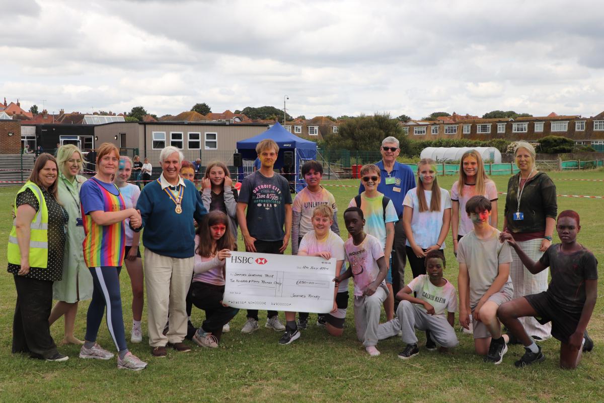 President Clive Livingstone presenting the donation to teacher Hannah Martin (in the striped top) who organised the event watched by painted students and teachers 