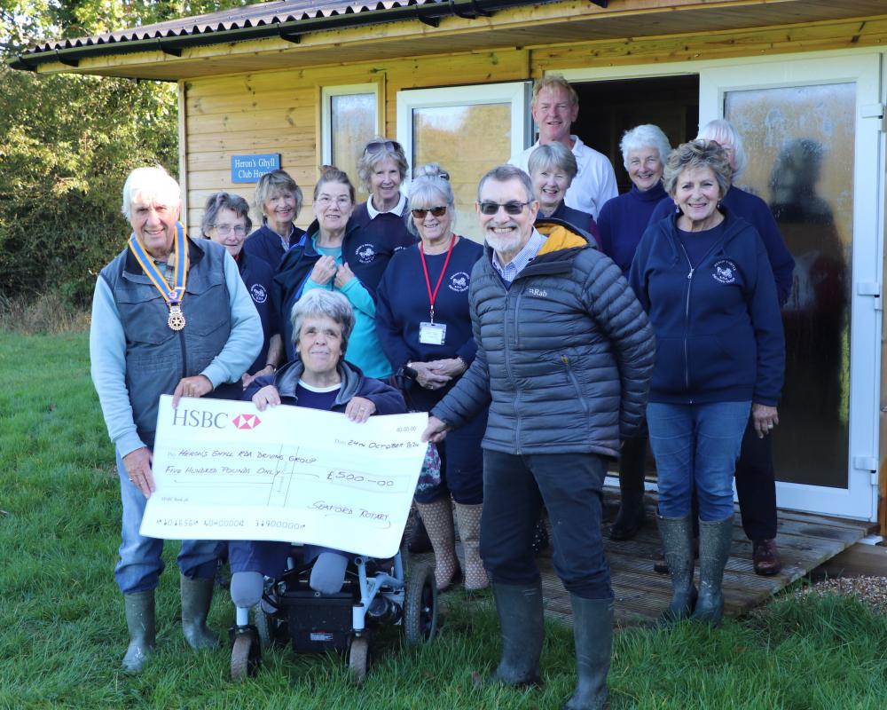 President Clive Livingstone and Tony Humphreys from Martello Rotary Club presenting the cheque to Heron’s Ghyll RDA Driving Group President Karen Tritton in front of the Club’s Clubhouse