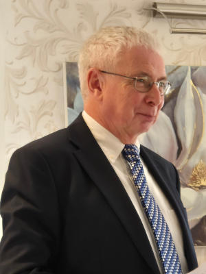 A white-haired man wearing glasses and a black suit