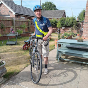 A man wearing a cycling helmet holding his bike on a garden patio