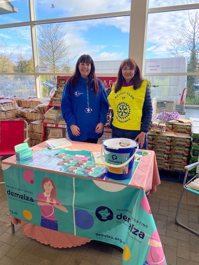 Two people behind a table with Demelza House charity collection materials