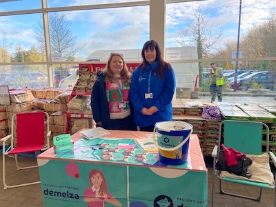 Two people behind a table with Demelza House charity collection materials